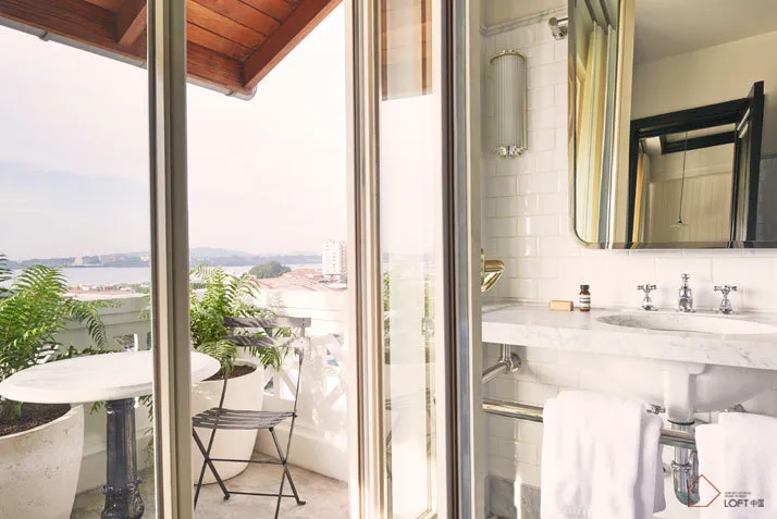 White tiled bathroom with a glass door and a balcony with a table and chairs.