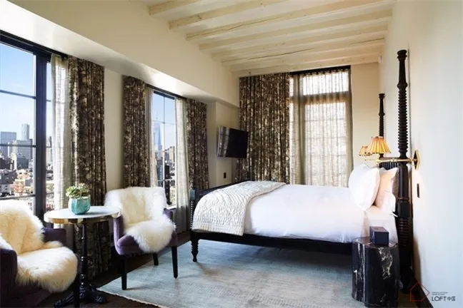 Modern bedroom featuring a bed with white linens, a fur-covered accent chair, and floral arrangement on a small round table w