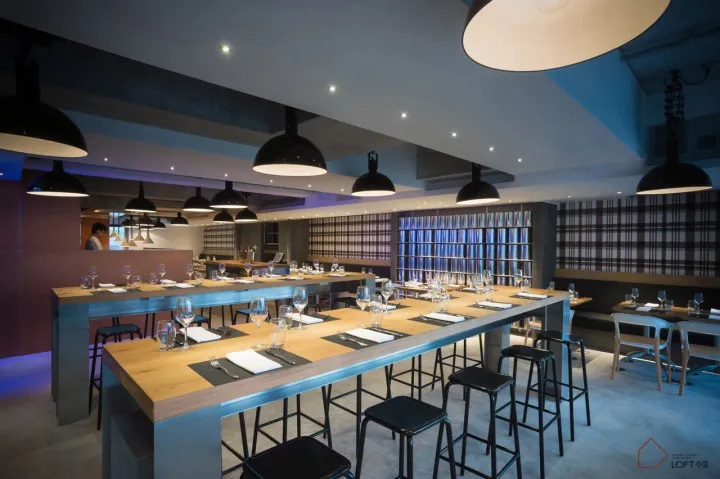 Modern industrial restaurant interior with wooden tables, metal stools, and glass paneling.