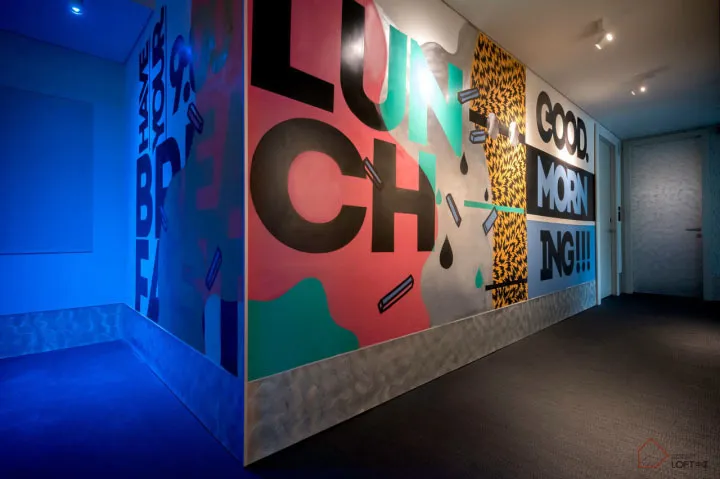 A vibrant, minimalist corridor featuring colorful graffiti-style mural art with phrases such as 'I HAVE YOUR BREAKFAST', 'GOO