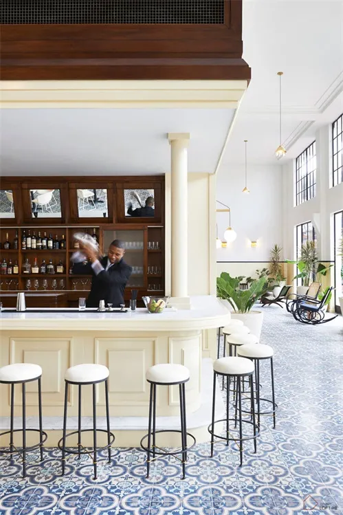 A modern restaurant bar with white floor tiles and a bartender preparing drinks.