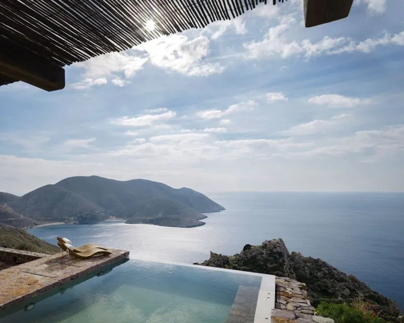 A scenic view of a vacation home featuring an infinity pool overlooking the ocean and distant mountains.