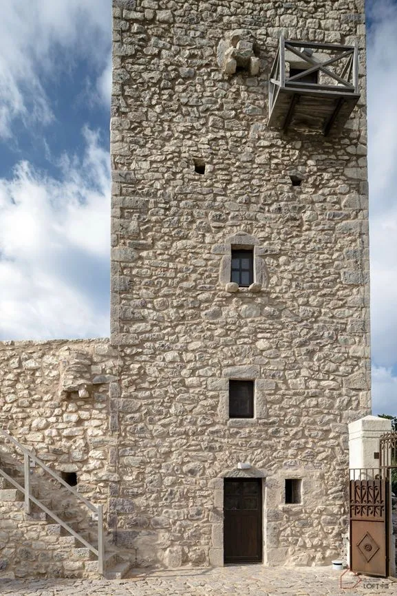 A tall, ancient stone tower with a wooden door and a wooden balcony.