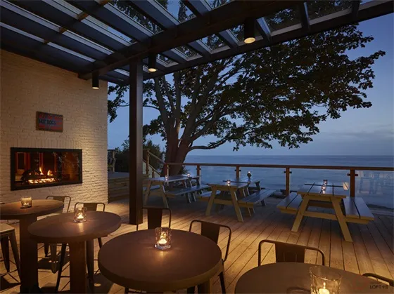 Industrial-style restaurant deck overlooking the bay with wooden tables and chairs, illuminated by candles.