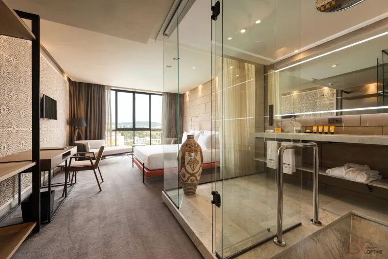Modern hotel bedroom suite featuring marble, glass, metal, and cloth elements.
