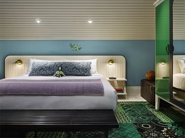 Modern hotel room with a king-size bed, green carpet, and blue accent wall.