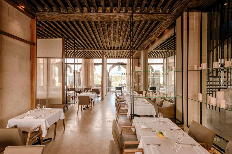 Modern restaurant interior with industrial-style decor featuring wooden ceiling, glass shelves, and concrete flooring.