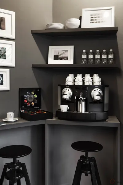 A minimalist coffee bar featuring a coffee machine with white cups and saucers on a black countertop, black stools, and decor