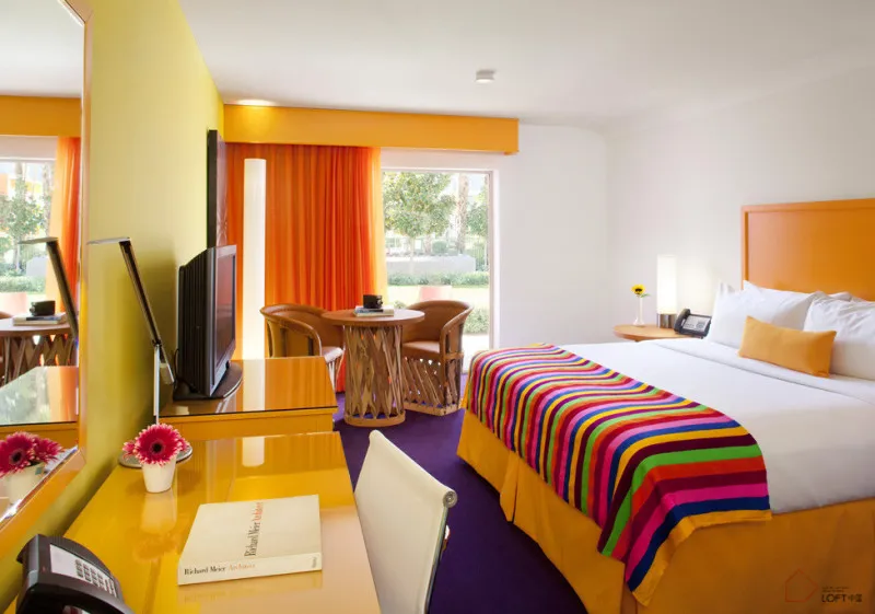 A modern hotel room featuring a bed with a colorful striped blanket, a wooden table, and various decor items.