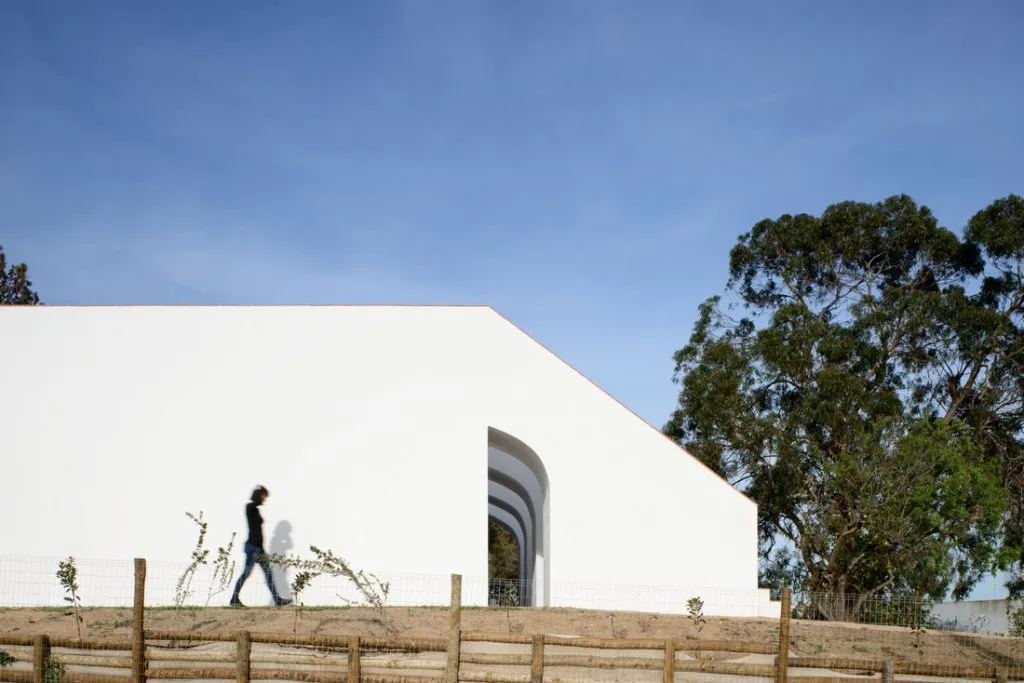 A modern residential building with a white concrete exterior, features large windows and an open archway, set against a clear