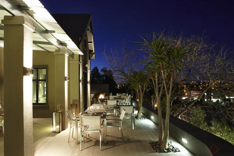 Terrace dining area with natural and artificial lighting, timber flooring, and granite countertops at night.
