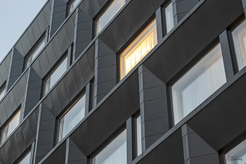 Modern apartment building with dark metal cladding and illuminated windows.