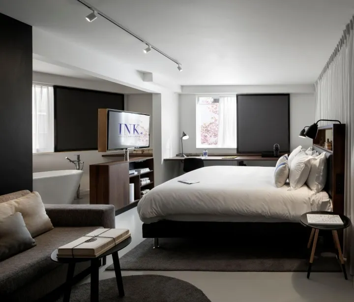 Modern, minimalist bedroom with a large bed, a cozy sofa, and a flat-screen TV.