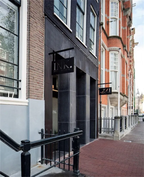 A view of a brick and concrete building with steel railings and a black sign with the text 'INK.'