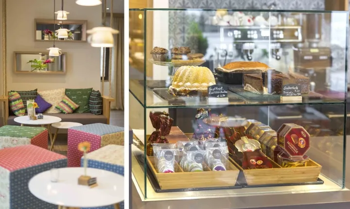 A cozy coffee shop interior with colorful cushions, a glass display case, and various pastries.