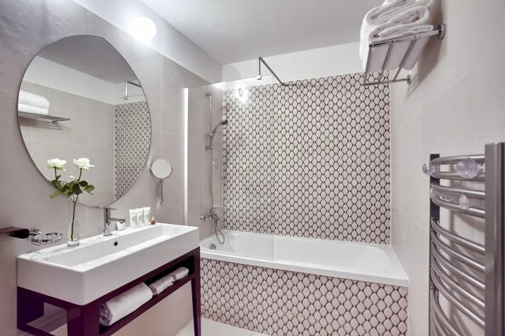 Modern minimalist bathroom with patterned ceramic tiles, featuring a walk-in shower, white vanity with sink, and a towel rack