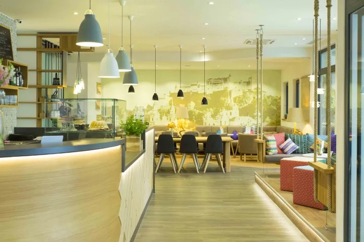 A casual cafe with modern design elements, featuring a long wooden counter, hanging lamps, and a seating area with colorful c