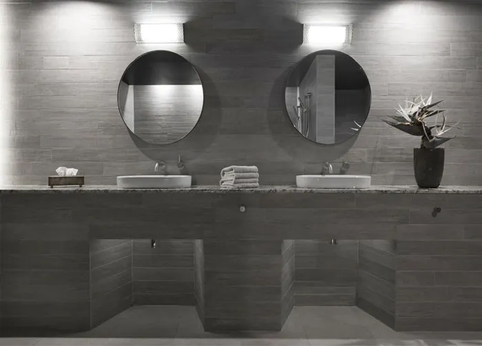 Modern bathroom with gray ceramic tiles, two sinks, and round mirrors.