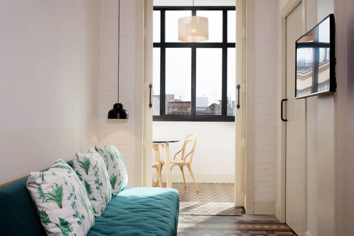 A minimalist living room featuring green plant-patterned throw pillows and brick walls painted in light colors.