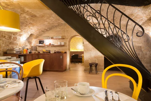 Modern cafe interior with wooden stairs, yellow chairs, and a rustic stone wall
