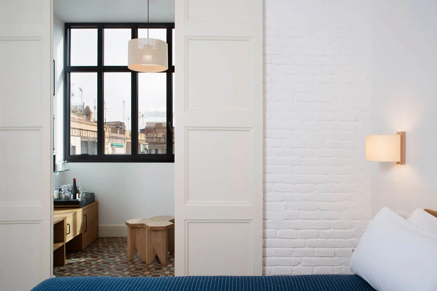 A minimalist bedroom featuring a white brick wall and a bed with a blue and white bedspread.