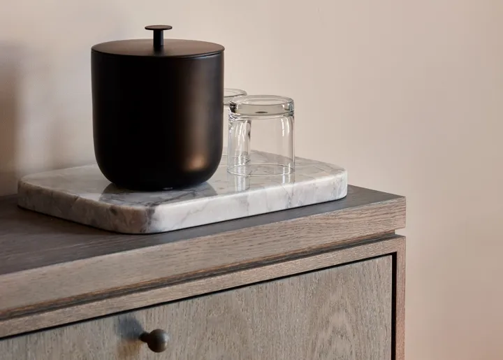 A modern marble side table with a black container and two transparent glasses.