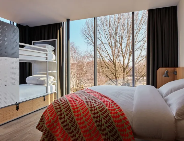 Modern minimalist bedroom featuring a bed with a white headboard and red and green geometric blanket, bunk beds, and large wi