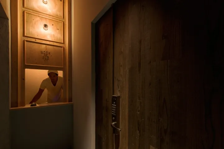 A wooden reception desk with a glass top and a man standing behind it in the dark.