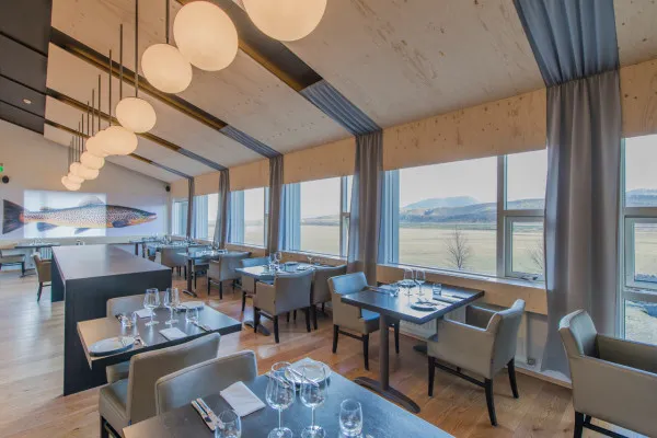 Industrial-style restaurant interior with wooden furnishings and large windows providing natural light.