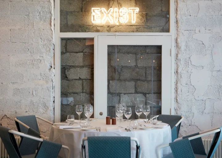 A restaurant interior with a rustic, industrial design featuring exposed brick walls, concrete floors, and a round dining tab