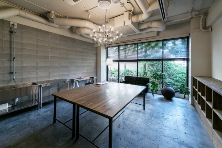 A modern conference room featuring a wooden table, concrete walls, and stainless steel fixtures, with a view of greenery outs