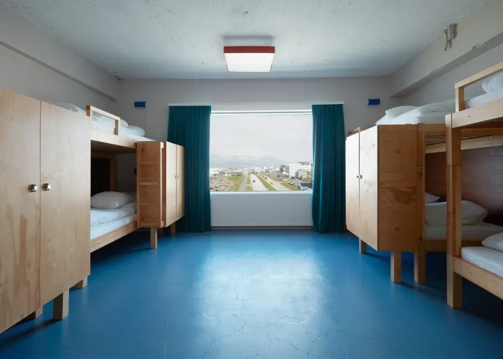 Modern minimalist bedroom featuring wooden bunk beds with view of cityscape through large windows.