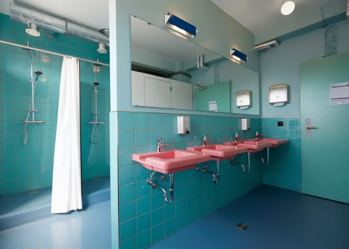 A modern public toilet with ceramic tile walls, pink sinks, and blue flooring.