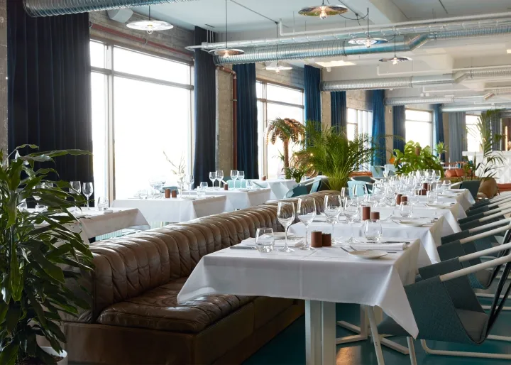 A modern restaurant interior filled with green plants and white tables.