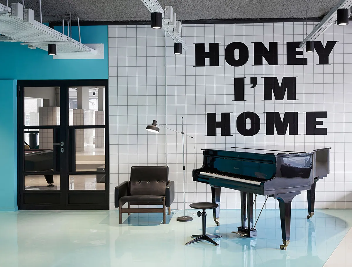 現代室內空間,白色瓷磚搭配黑色點綴,以及一台印有「Honey I'm Home」字樣的黑色三角鋼琴。