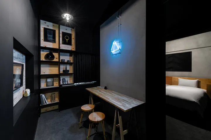 A minimalist bedroom with a wooden headboard and a wooden table in front of a wall mounted with books and decorative objects.