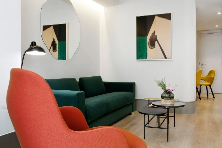 A minimalist living room featuring a green sofa, orange armchair, and modern art