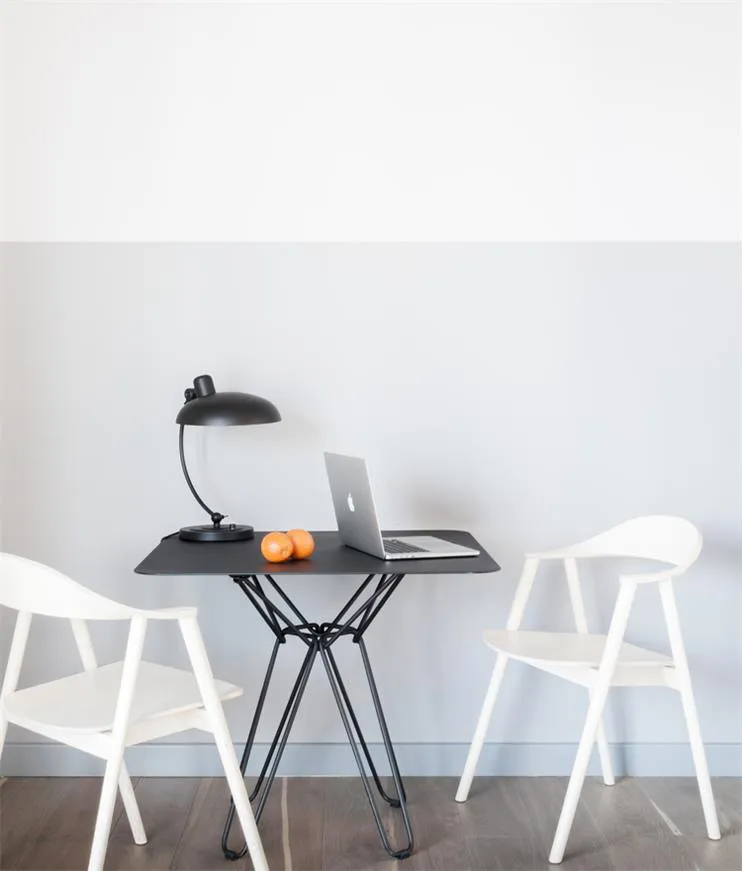 Minimalist workspace featuring a black metal table with a laptop, desk lamp, and oranges.