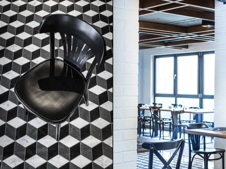 A black and white geometrically patterned tile floor in a restaurant interior with wooden chairs and white walls.
