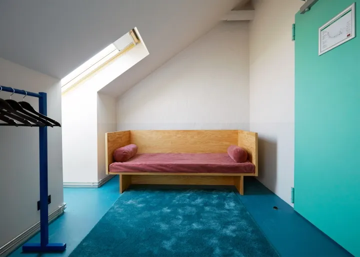 A minimalist bedroom with a wooden bench, a blue floor, and a window.