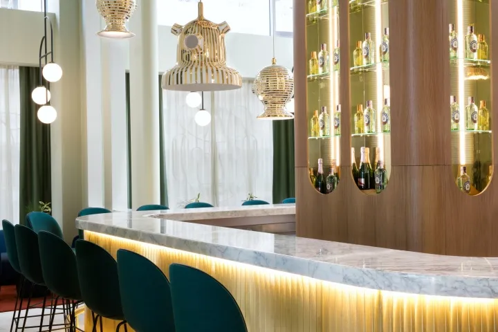 Modern restaurant bar interior with marble countertops, wooden seating, and glass bottles.