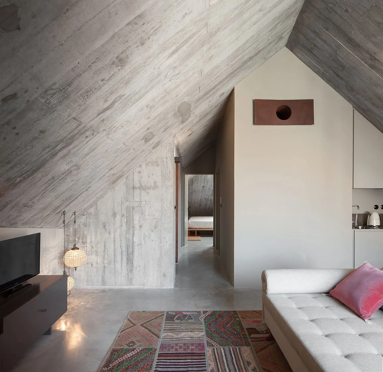 Concrete minimalist living room with a white couch and colorful rug.