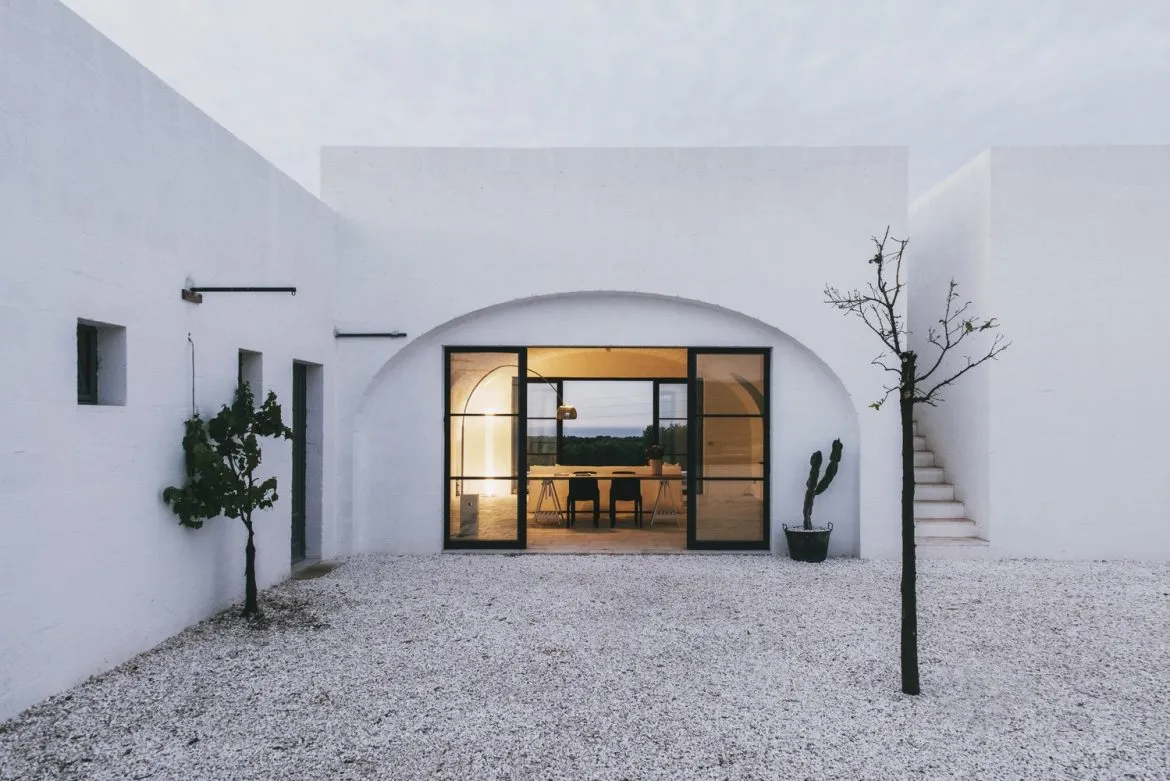 A minimalist white building with large windows and a gravel courtyard.