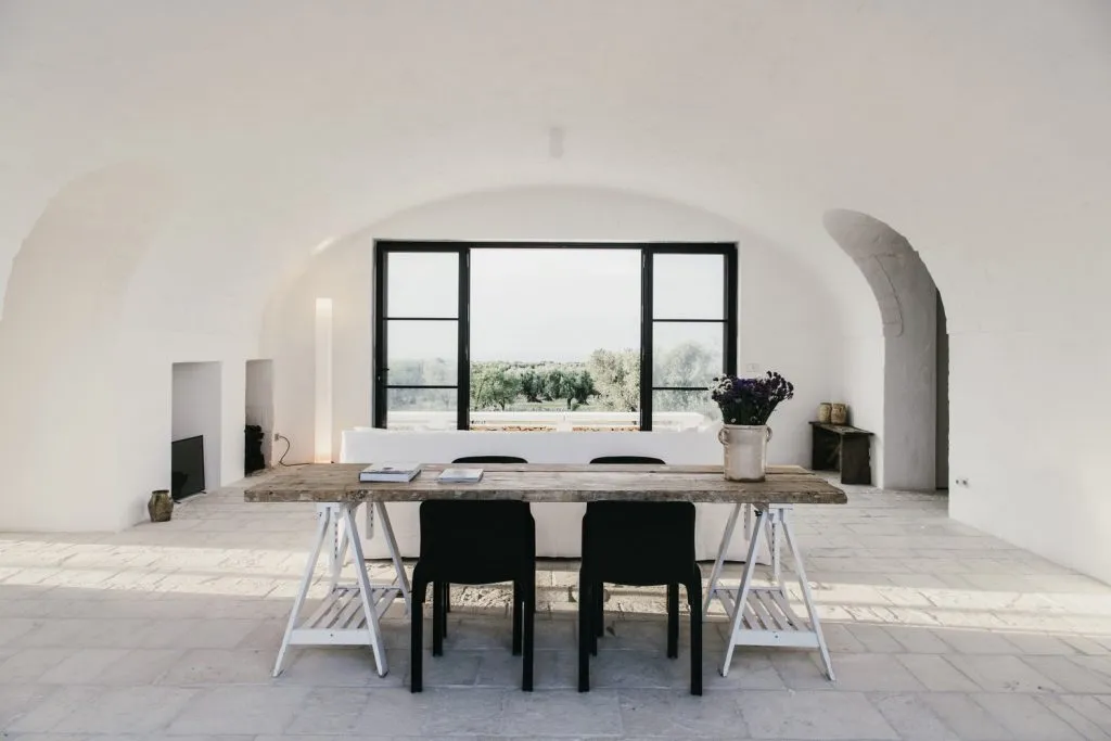 A modern industrial dining room with cement walls, wooden table, and black chairs and accents.