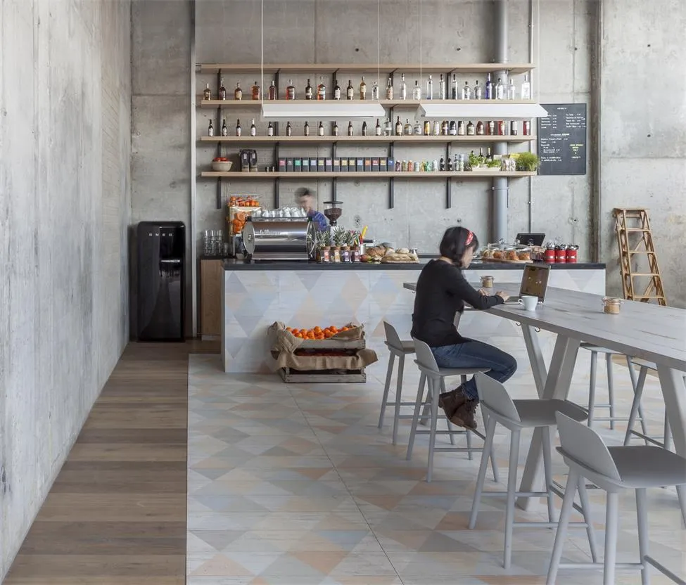 Modern cafe bar with concrete walls, wooden tables, and seating arranged around a central bar counter.