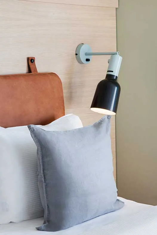A minimalist bedroom with a gray cushion, a leather headboard, and a modern lamp on the wall.