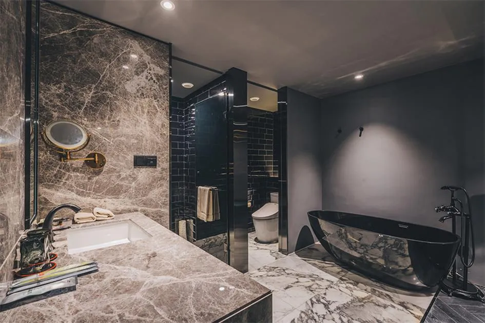 A modern bathroom featuring a marble sink, black bathtub, and black tiles.