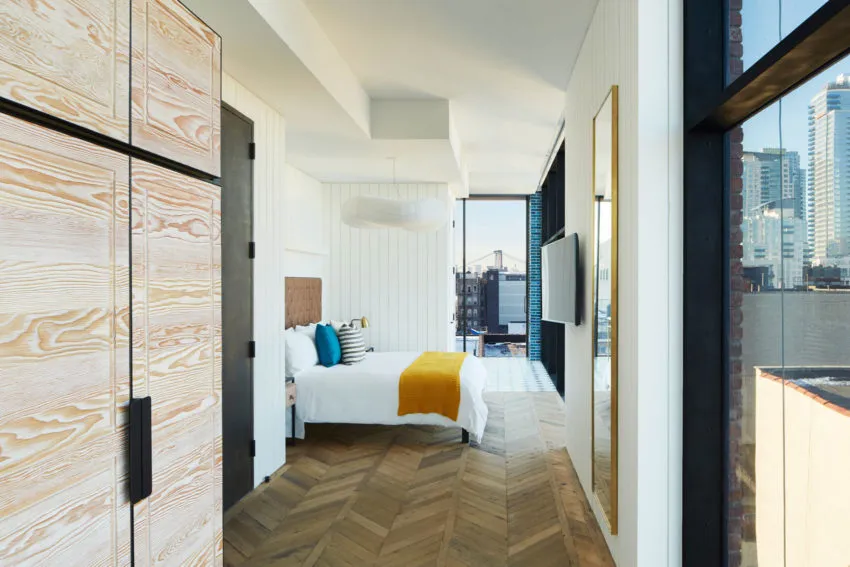 Modern bedroom interior with a bed, wardrobe, and large window overlooking the city.