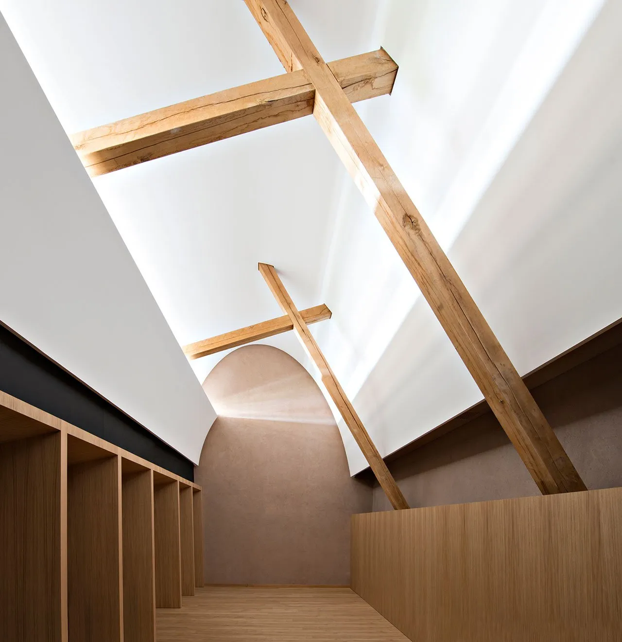 Interior of a modern building with wooden ceiling beams and light streaming through a large window.