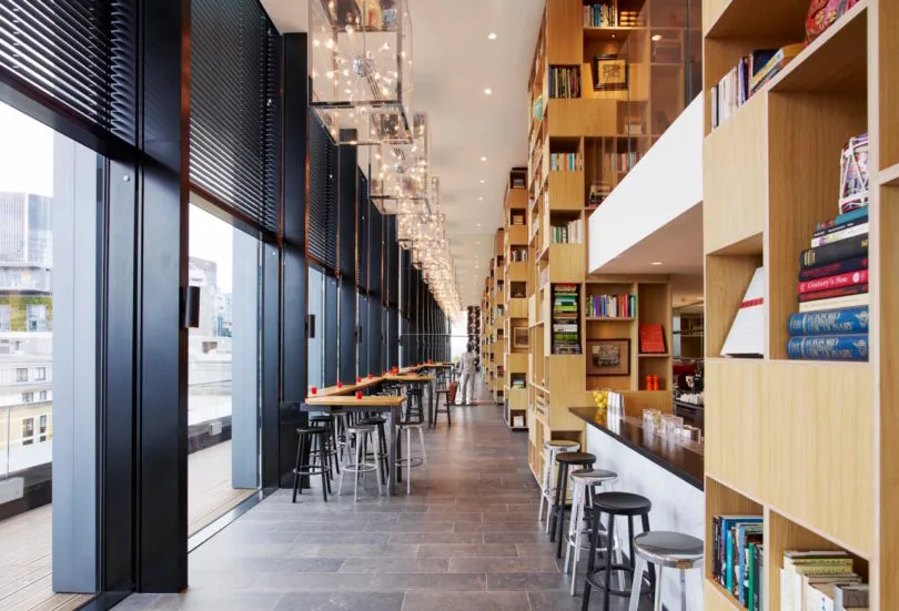 A spacious modern library cafe with wooden shelves and concrete flooring.